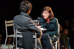 Production photo from Julius Caesar. Taken from behind Ben Whishaw we see him and the front of Michelle Fairley sat opposite each other. Michelle is leaning in as if to talk in secret to Ben.