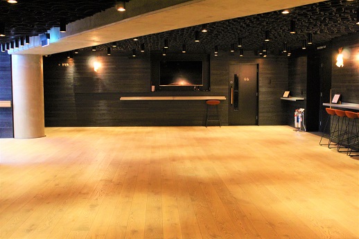 Picture of our lower foyer space, there are light laminate flooring, a television screen on the wall at the back and some high stools on the right. There is light coming in from the left from our main foyer.