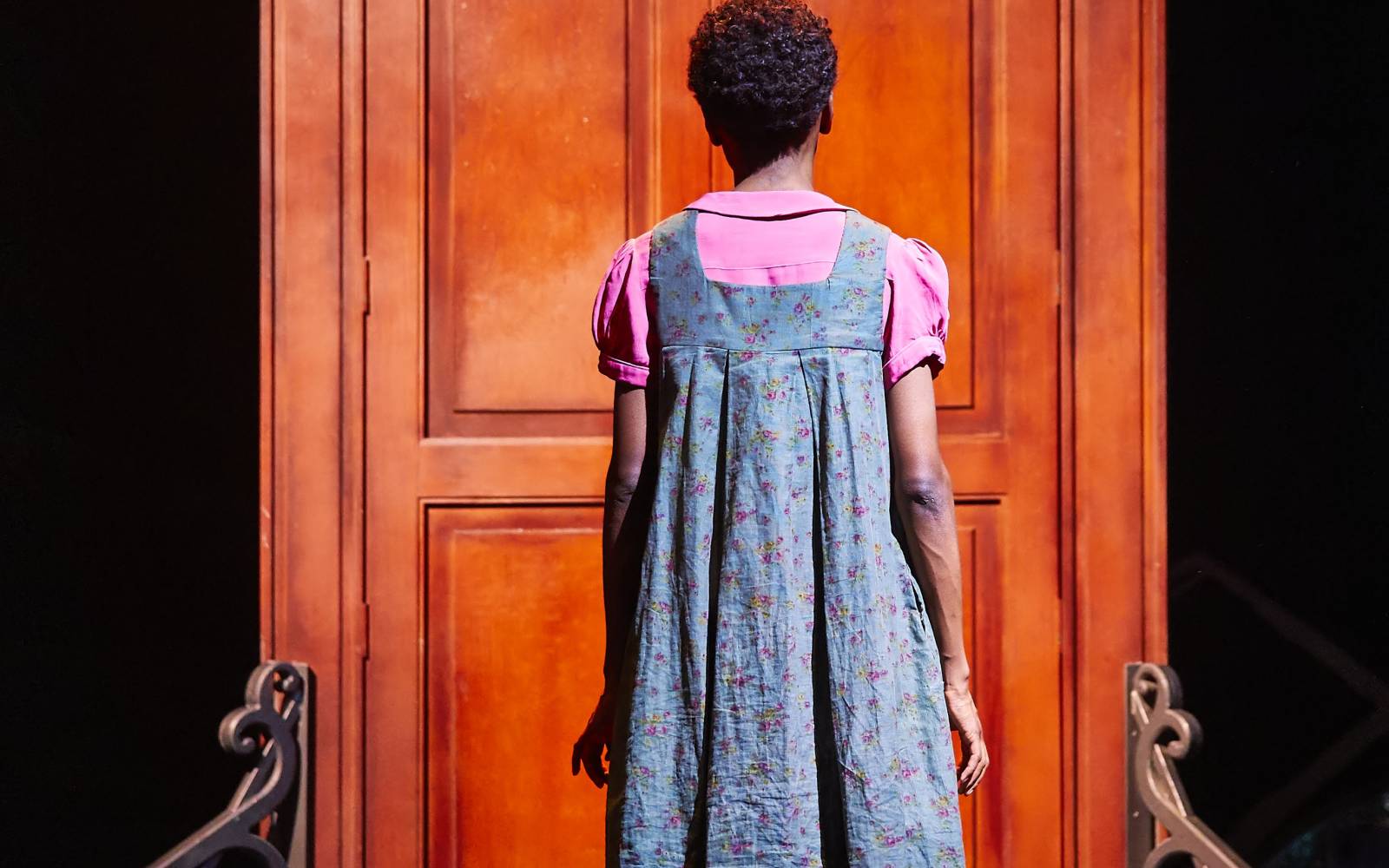 A woman seen from behind. She stands in front of a large wooden door