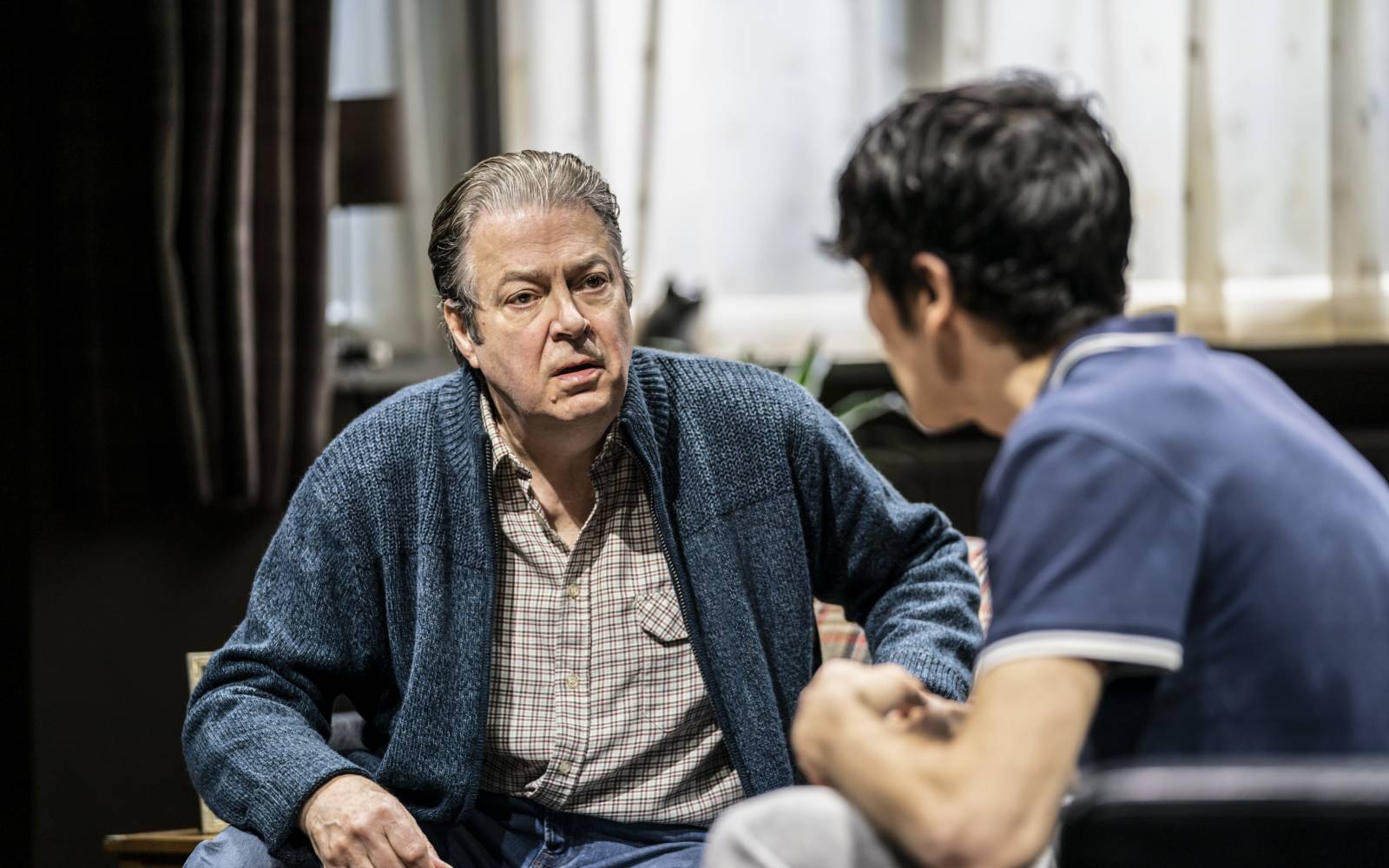 Roger Allam as Salter talks to Colin Morgan as his sons. Both are sitting, in modern dress
