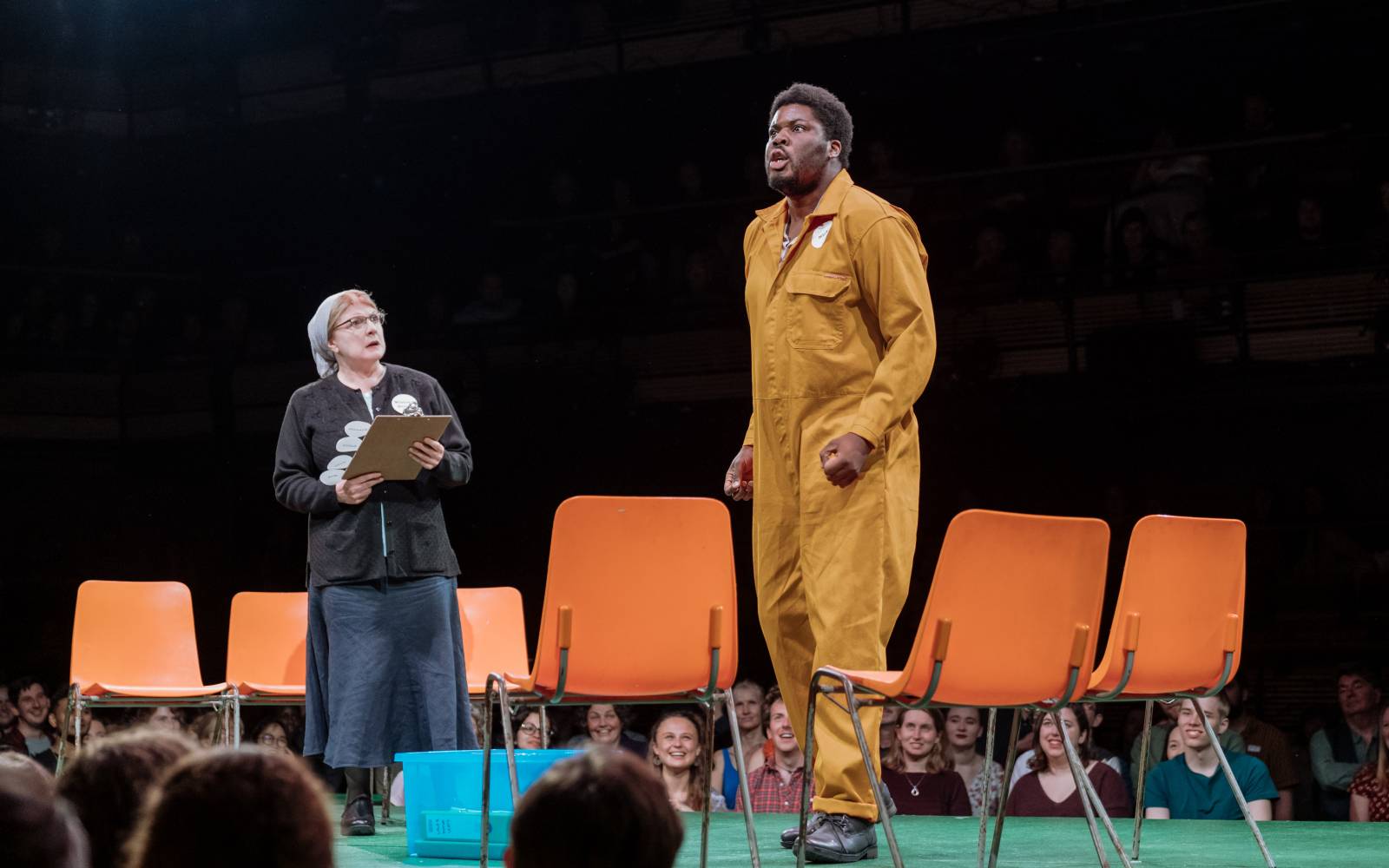 Hammed Animashaun (Bottom) performs, as Felicity Montagu (Quince) watches. They are surrounded by plastic chairs