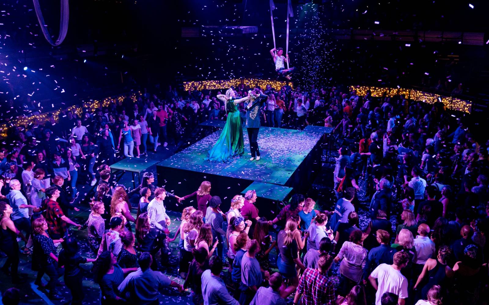 Gwendoline Christie (Titania) and Oliver Chris (Oberon) dance together under falling confetti, surrounded by a crowd