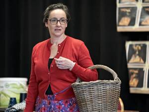 Photo of Pandora Colin. She's wearing a red cardigan buttoned in the middle, dark framed glasses and holding a wicker basket on her arm.