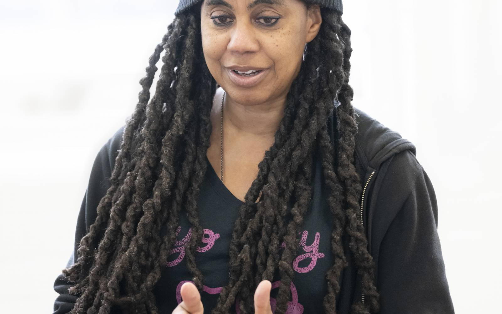 Photo of Suzan-Lori Parks (long black twisted braids, black beanie, black zipped hoodie). She's deep in explanation, with both hands out in front of her as if describing something.