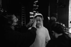 Julie Atherton (white nuns costume) stands backstage as a member of the crew tucks her hair into her hood.