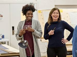 Dani Mosely (black hair, hoop earrings and a grey cardigan over a burgundy tshirt) and Mary Stewart (brown hair, navy top) stand laughing.