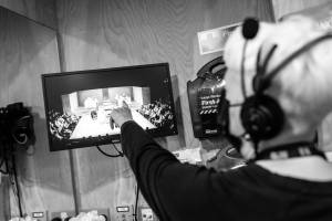 A screen in a dressing room shows what is happening on stage, it is being pointed at by a person with a headset.