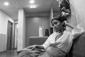 Alisha Bailey sits backstage on a sofa. She wears a short curled wig with a shirt and long skirt.