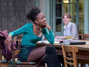 Racheal Ofori sits at a table, she wears a long sleeved top with a sparkling green skirt.
