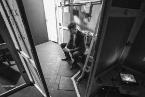 Josh Finan sits on a step in the wings next to a door that leads to the stage.