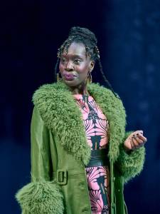 Ony Uhiara stands wearing a green coat with a patterned pink dress.