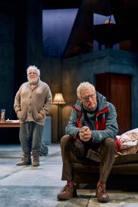 Simon Russell Beale stands with his hands in his pockets, he wears an old beige cardigan. Michael Simkins sits with his hands clasped in front of him, he does not face Simon.