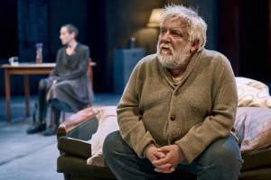 Simon Russell Beale sits with his hands clasped in front of him, he looks thoughtful.
