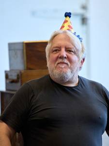 Simon Russell Beale wears a black t shirt and a spotted party hat.