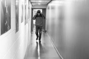 Michael Simkins walks along a corridor wearing a bike helmet and waterproof coat