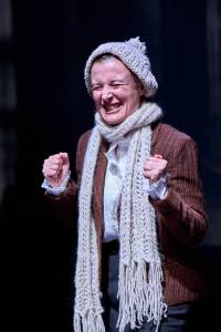 Lyndsey Marshal smiles in delight with her fist closed in excitement. She wears a wooly hat and scarf over jacket.