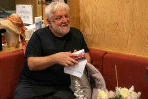 A man (Simon Russell Beale) is sat on a sofa opening a card, smiling