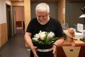 A man (Simon Russell Beale) is holding a hat box of festive flowers
