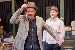 Danny Mays smiles widely with a hand on his trilby hat.
