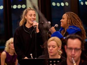 Celinde Schoenmaker and Marisha Wallace look at each other smiling and sing together.