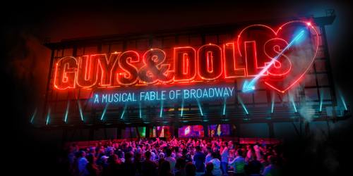 A neon sign is brightly lit in red. It reads Guys & Dolls, followed by a red heart pierced by a blue arrow. Below the sign, a crowd of people gather