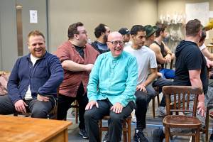 The cast of Guys & Dolls sit laughing with each other in rehearsals.