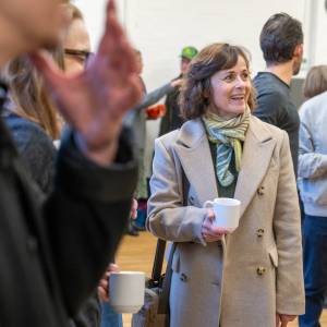 Amanda Root holding a white cup and smiling amidst a group of people.